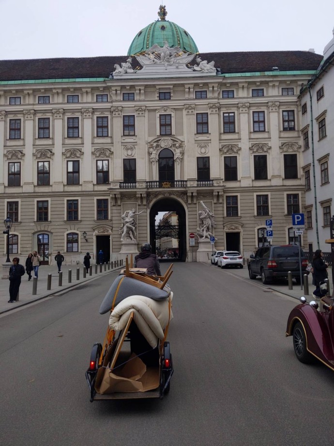 Another photo of the mattress-and-upside-down-chair cargo bike transport passing through the courtyard of Hofburg