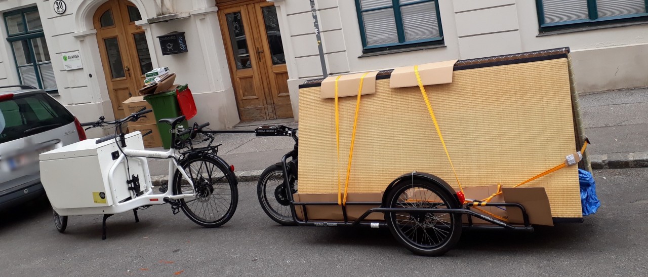 The cargo bike from earlier, carrying Tatami mats, this time parked next to a car in a regular side street, shown from the side