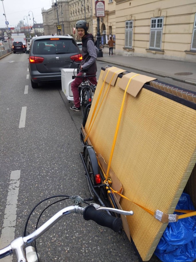 Myself, half-standing, half-sitting, in between my cargo bike, cargo trailer and cars on the middle lane of a three-lane street next to Vienna's Museumsquartier