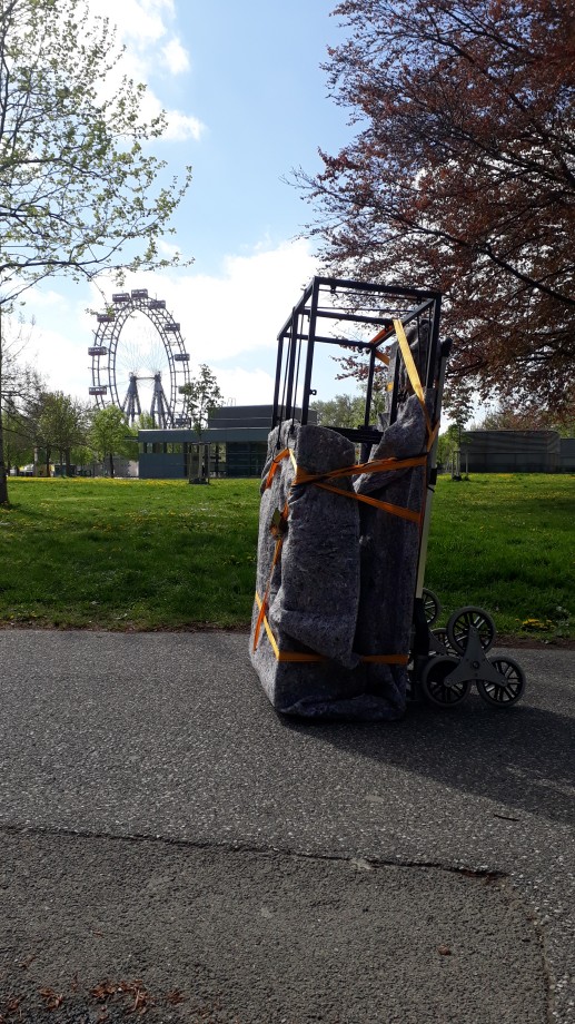 The hand truck from earlier, carrying a cupboard, in front of a lush green meadow and Vienna's giant ferris wheel